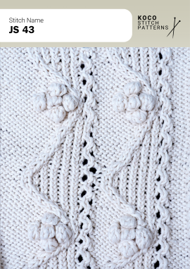 Framed bobble accents and delicate cables bring soft dimension to this elegant handknit panel Close-up of the JS 43 handknit stitch pattern in white yarn, showing raised bobble motifs framed by cable columns and small eyelet lace openings
