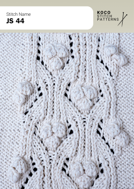 Raised bobbles, flowing cables, and lace details create a richly textured handknit design Close-up of the JS 44 handknit stitch pattern in white yarn, featuring raised bobble motifs, flowing cables, and eyelet lace details